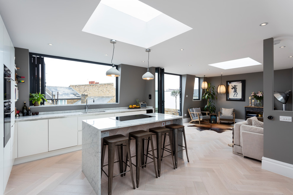 Mid-sized contemporary l-shaped eat-in kitchen in London with flat-panel cabinets, white cabinets, marble benchtops, light hardwood floors, with island and beige floor.