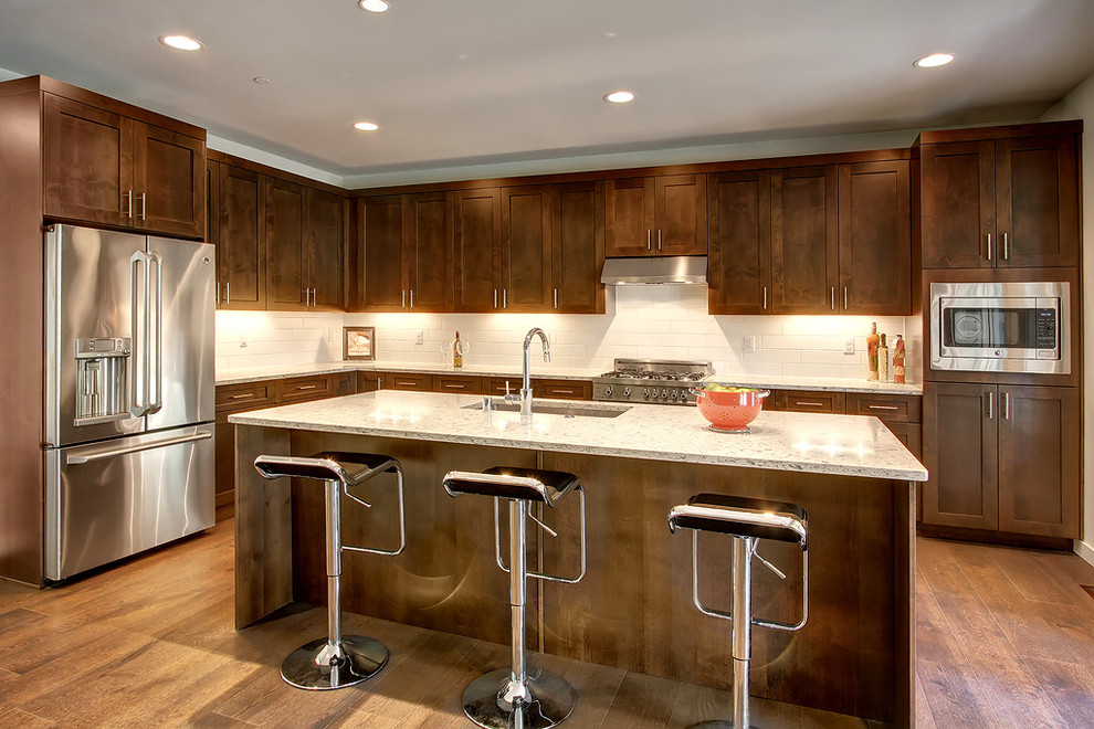 Open concept kitchen - transitional l-shaped dark wood floor open concept kitchen idea in Seattle with a drop-in sink, shaker cabinets, dark wood cabinets, quartz countertops, white backsplash, ceramic backsplash, stainless steel appliances and an island