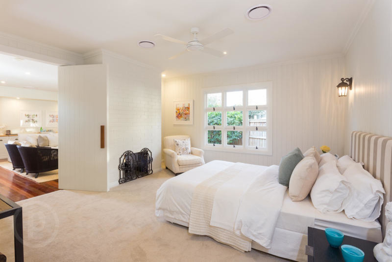 Photo of a large contemporary master bedroom in Brisbane with white walls, carpet, a standard fireplace, a brick fireplace surround and beige floor.