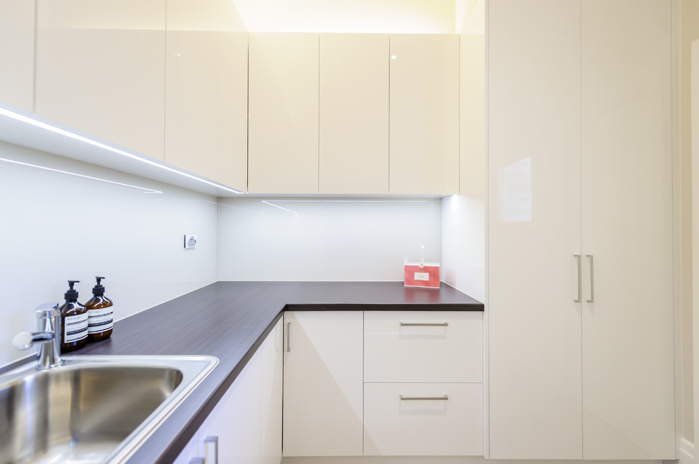 Mid-sized contemporary l-shaped dedicated laundry room in Melbourne with a drop-in sink, flat-panel cabinets, beige cabinets, laminate benchtops, concrete floors and a stacked washer and dryer.