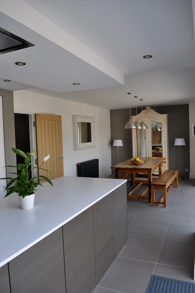 This is an example of a medium sized galley kitchen/diner in London with a submerged sink, flat-panel cabinets, white cabinets, composite countertops, white splashback, black appliances, porcelain flooring and an island.