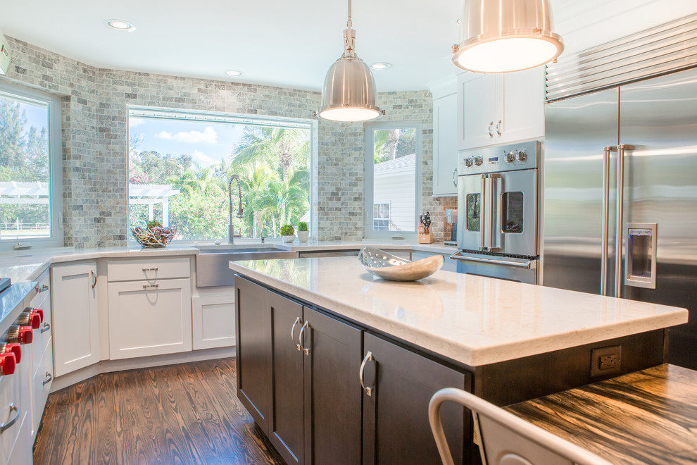 Example of a large transitional u-shaped medium tone wood floor open concept kitchen design in Miami with a farmhouse sink, shaker cabinets, white cabinets, quartz countertops, multicolored backsplash, stone tile backsplash, stainless steel appliances and an island