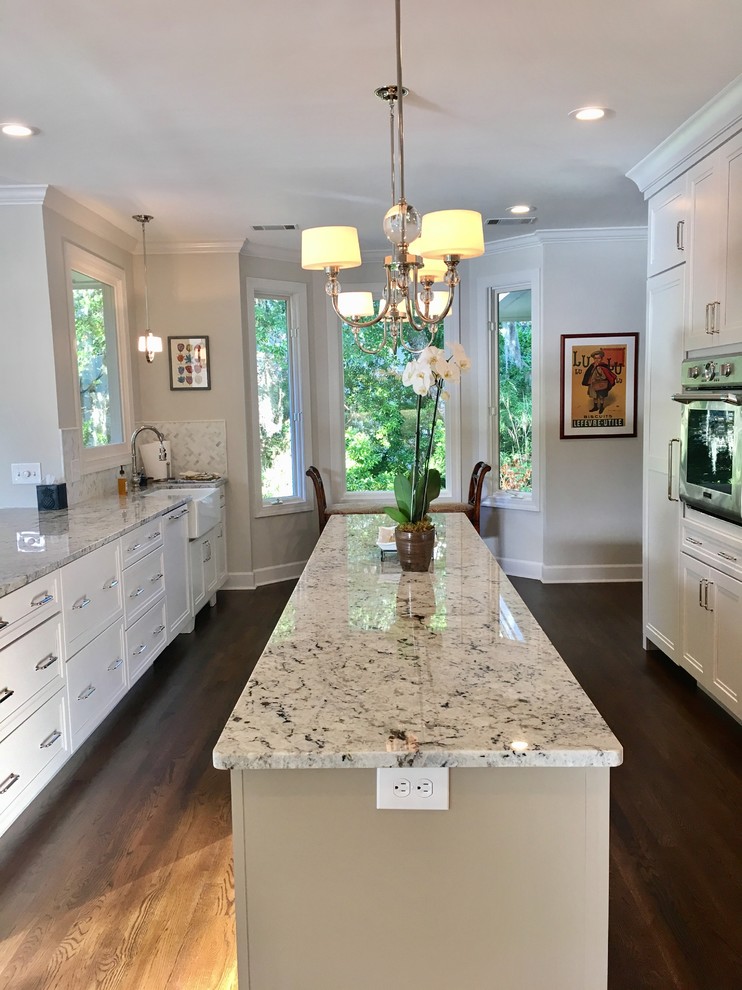 Eat-in kitchen - large transitional u-shaped dark wood floor and brown floor eat-in kitchen idea with a farmhouse sink, recessed-panel cabinets, beige cabinets, granite countertops, white backsplash, marble backsplash, stainless steel appliances and an island