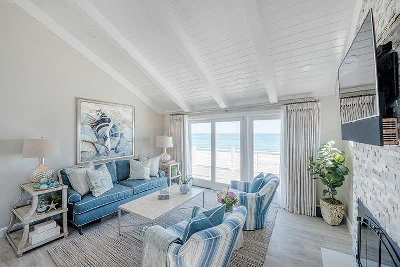 This is an example of a mid-sized beach style open concept family room in Boston with beige walls, a standard fireplace, a stone fireplace surround, a wall-mounted tv, light hardwood floors and beige floor.