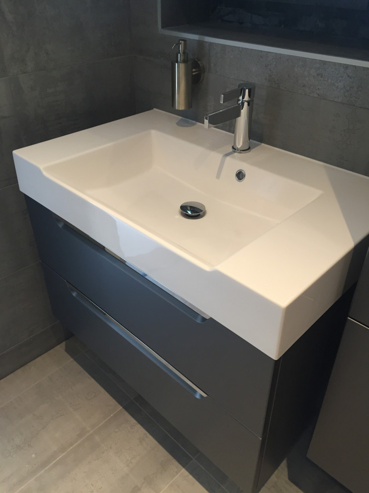 This is an example of a large industrial master wet room bathroom in London with beaded inset cabinets, black cabinets, a wall-mount toilet, gray tile, porcelain tile, grey walls, porcelain floors, a wall-mount sink, grey floor, a sliding shower screen, a double vanity and a floating vanity.