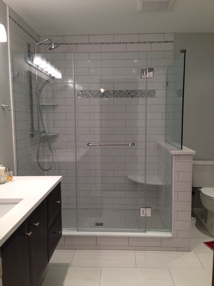 Mid-sized traditional 3/4 bathroom in Philadelphia with flat-panel cabinets, dark wood cabinets, a corner shower, a two-piece toilet, white tile, porcelain tile, grey walls, porcelain floors, an undermount sink and solid surface benchtops.