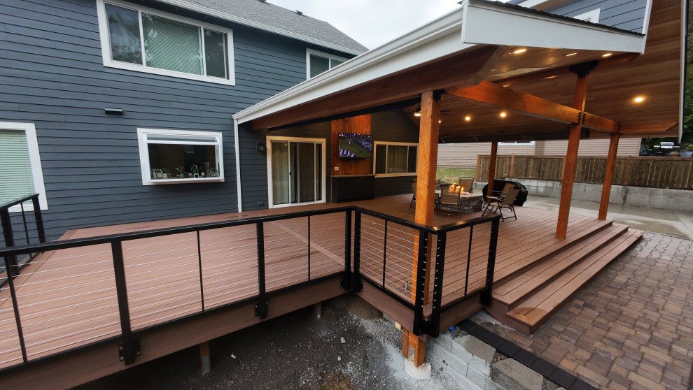 Example of a large arts and crafts backyard ground level cable railing deck design in Seattle with a roof extension