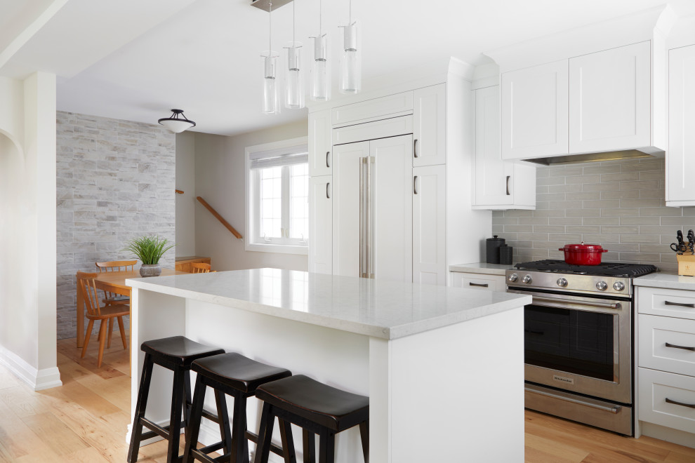 Inspiration for a mid-sized transitional light wood floor and beige floor kitchen remodel in Toronto with a single-bowl sink, shaker cabinets, white cabinets, quartz countertops, gray backsplash, porcelain backsplash, paneled appliances, an island and white countertops