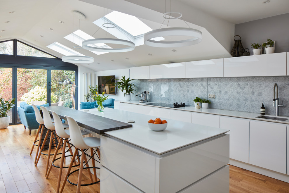 Design ideas for a large modern galley kitchen/diner in London with a built-in sink, flat-panel cabinets, white cabinets, granite worktops, grey splashback, metal splashback, integrated appliances, dark hardwood flooring, an island, brown floors and white worktops.
