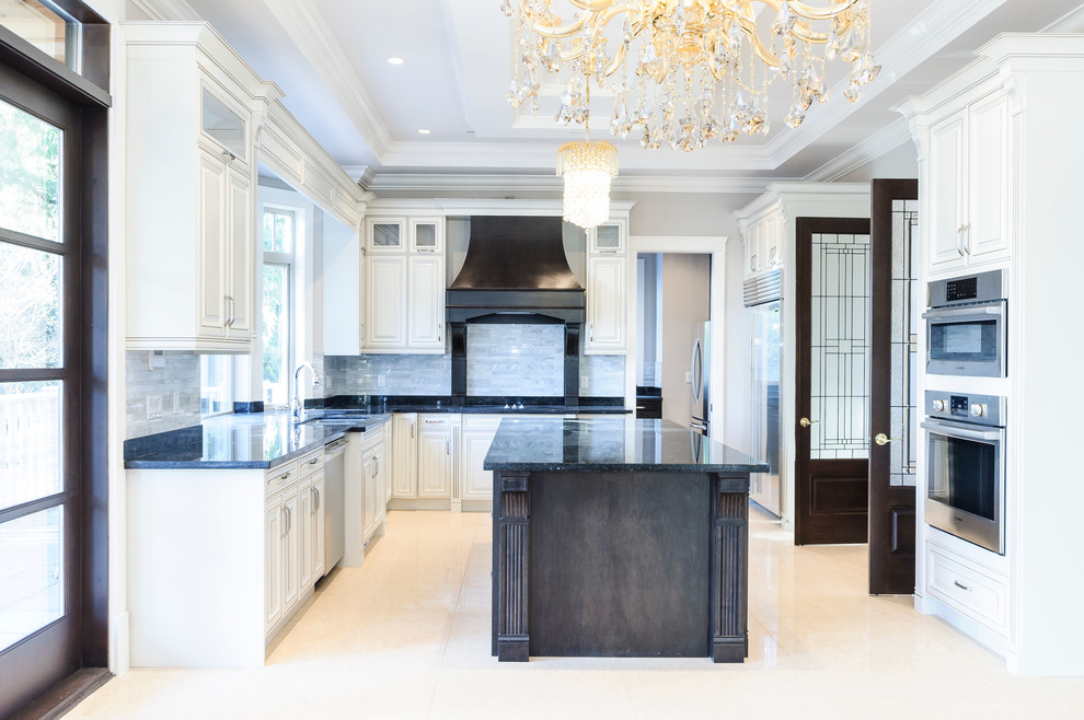 This is an example of a mid-sized traditional u-shaped eat-in kitchen in Vancouver with an undermount sink, raised-panel cabinets, granite benchtops, grey splashback, stone tile splashback, stainless steel appliances, travertine floors, with island, white cabinets and beige floor.