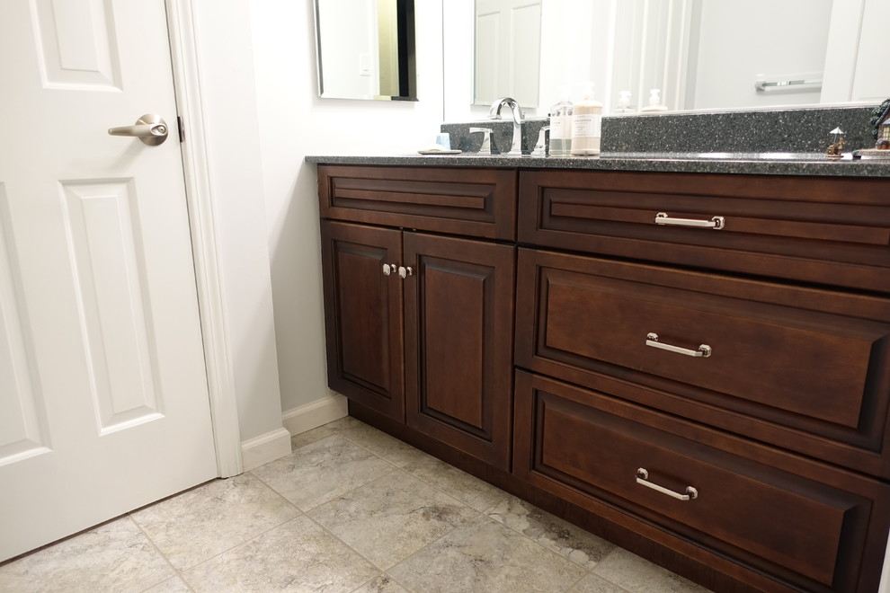 Photo of a traditional bathroom in Other with an integrated sink, raised-panel cabinets, dark wood cabinets, solid surface benchtops, beige tile, ceramic tile and ceramic floors.
