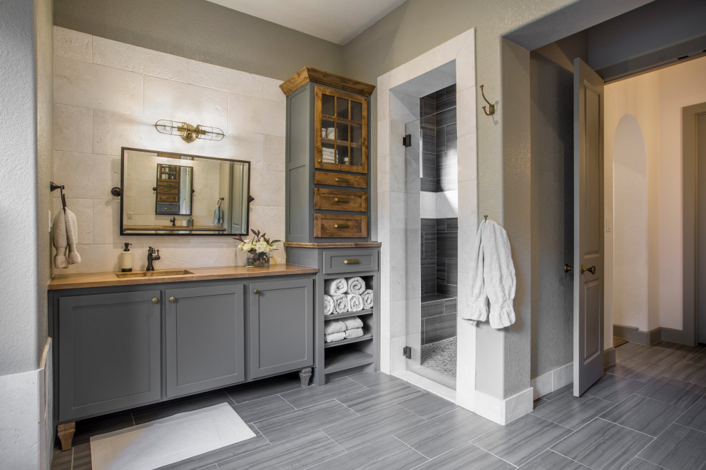 Design ideas for a mid-sized traditional master bathroom in Dallas with grey cabinets, a freestanding tub, a curbless shower, a two-piece toilet, white tile, marble, porcelain floors, an undermount sink, wood benchtops, grey floor, a hinged shower door, brown benchtops, a double vanity, a built-in vanity, decorative wall panelling, shaker cabinets and green walls.