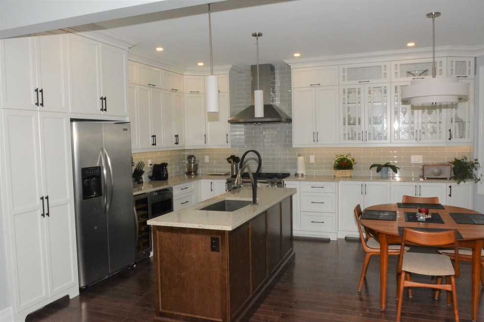 This is an example of a large traditional l-shaped eat-in kitchen in Toronto with an undermount sink, shaker cabinets, white cabinets, quartz benchtops, grey splashback, subway tile splashback, stainless steel appliances, dark hardwood floors and with island.