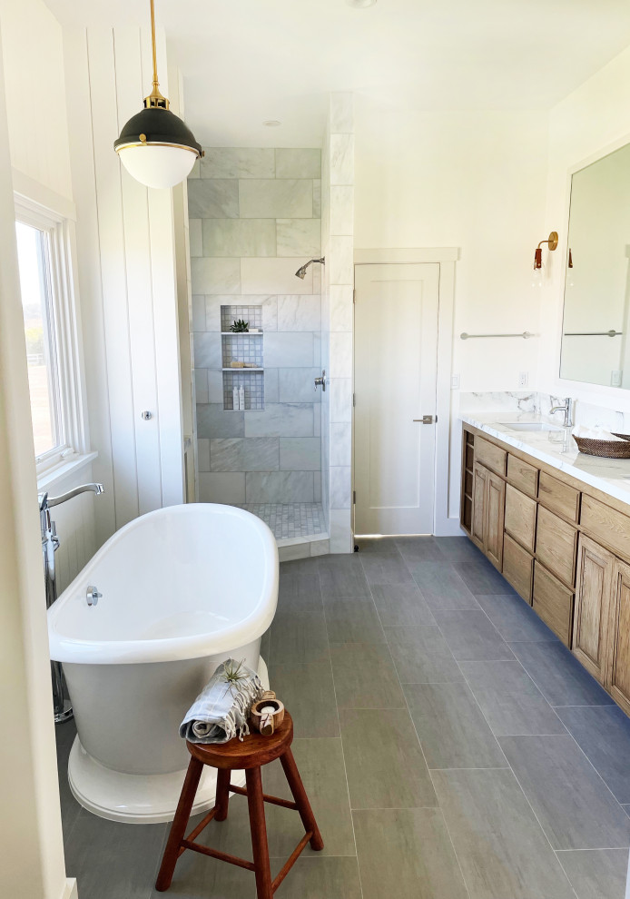 Inspiration for a large country master bathroom in Santa Barbara with raised-panel cabinets, medium wood cabinets, a freestanding tub, a corner shower, white tile, marble, white walls, porcelain floors, an undermount sink, marble benchtops, grey floor, an open shower, white benchtops, an enclosed toilet, a double vanity, a built-in vanity and decorative wall panelling.