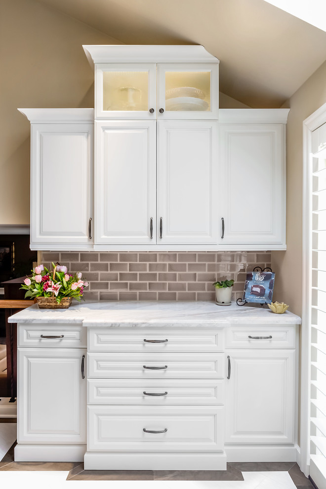 Kitchen pantry - mid-sized transitional u-shaped porcelain tile and white floor kitchen pantry idea in Seattle with an undermount sink, raised-panel cabinets, white cabinets, marble countertops, brown backsplash, subway tile backsplash, stainless steel appliances, an island and white countertops