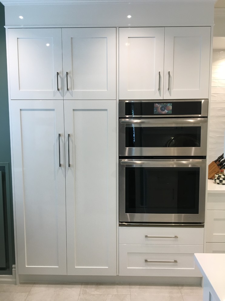 Photo of a mid-sized contemporary galley separate kitchen in Toronto with an undermount sink, shaker cabinets, white cabinets, quartz benchtops, white splashback, ceramic splashback, stainless steel appliances, porcelain floors, no island and white floor.