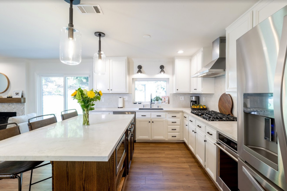 This is an example of a mid-sized modern galley eat-in kitchen in Los Angeles with an undermount sink, black cabinets, quartzite benchtops, grey splashback, engineered quartz splashback, stainless steel appliances, vinyl floors, with island, brown floor and white benchtop.