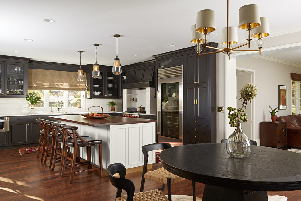 Photo of a large traditional l-shaped eat-in kitchen in Other with black cabinets, quartzite benchtops, white splashback, subway tile splashback, stainless steel appliances, dark hardwood floors, with island, an undermount sink, brown floor, white benchtop and recessed-panel cabinets.