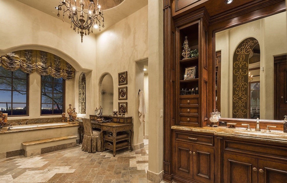 Inspiration for a large mediterranean master bathroom in Phoenix with recessed-panel cabinets, dark wood cabinets, a drop-in tub, an open shower, a one-piece toilet, beige tile, stone slab, beige walls, travertine floors, a drop-in sink and granite benchtops.
