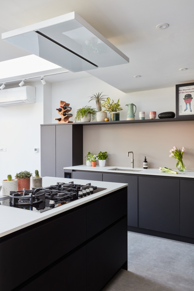 This is an example of a mid-sized modern u-shaped eat-in kitchen in London with an integrated sink, flat-panel cabinets, black cabinets, quartz benchtops, pink splashback, glass sheet splashback, stainless steel appliances, with island and white benchtop.