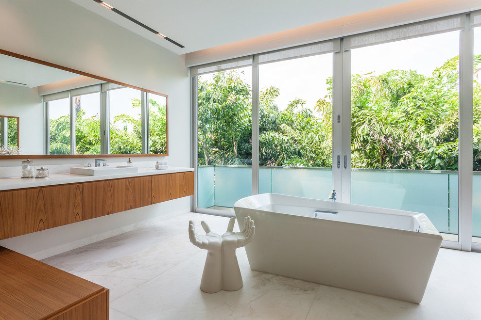 Photo of a contemporary bathroom in Miami with a drop-in sink, flat-panel cabinets, medium wood cabinets, a freestanding tub and white walls.
