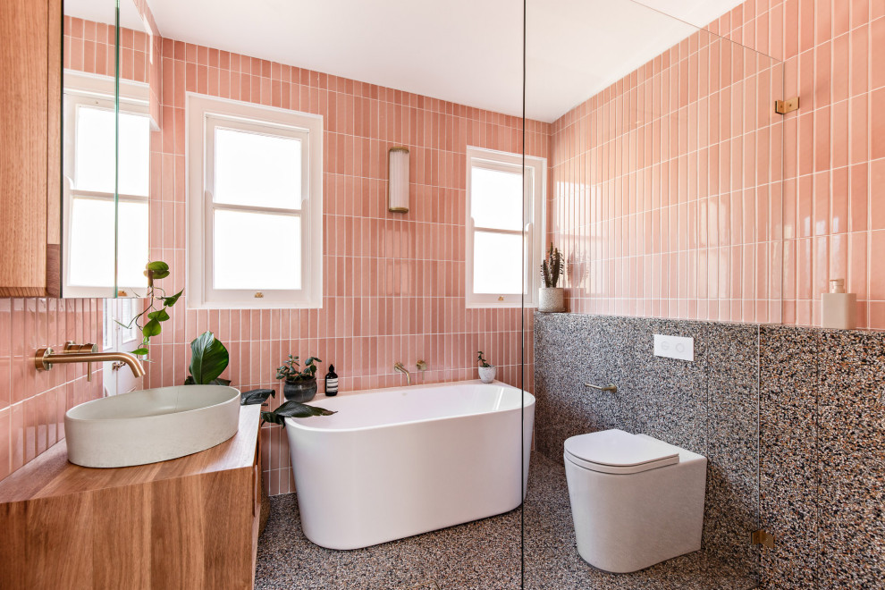 Inspiration for a mid-sized scandinavian master bathroom in Sydney with medium wood cabinets, a freestanding tub, an open shower, a two-piece toilet, pink tile, ceramic tile, pink walls, terrazzo floors, a wall-mount sink, wood benchtops, multi-coloured floor, an open shower, brown benchtops, a single vanity and a floating vanity.