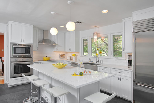 Bright white kitchen with shaker-style kitchen cabinet units, a large quartz island with four stools, stainless steel appliances, subway-tile backsplash, and globe pendants by sunny windows.