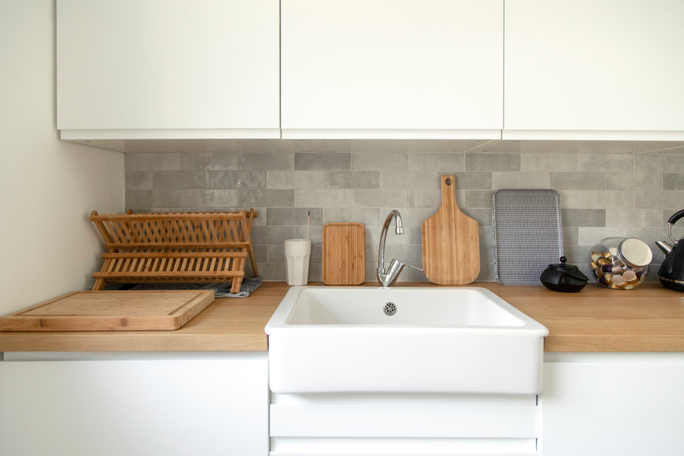 Photo of a mid-sized modern single-wall separate kitchen in Other with a farmhouse sink, flat-panel cabinets, white cabinets, wood benchtops, grey splashback, matchstick tile splashback, panelled appliances, cement tiles, no island, blue floor and brown benchtop.