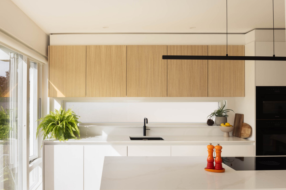 This is an example of a Scandinavian kitchen in Dublin With an Integrated Sink, White Cabinets, Quartz Worktops, Black Appliances, Light Hardwood Flooring and White Worktops.