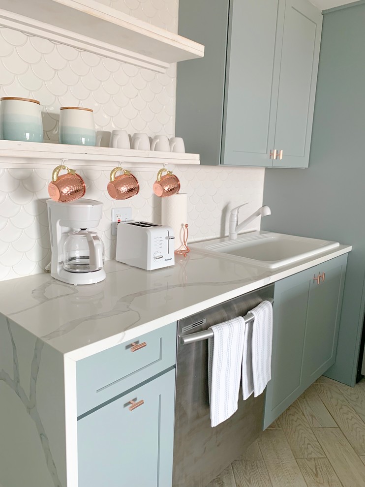 Photo of a beach style galley eat-in kitchen in Other with a drop-in sink, raised-panel cabinets, blue cabinets, quartz benchtops, white splashback, ceramic splashback, stainless steel appliances, cement tiles, a peninsula, beige floor and white benchtop.
