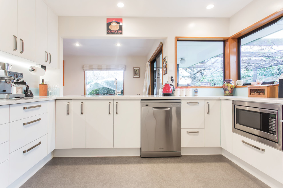 Photo of a large contemporary u-shaped separate kitchen in Christchurch with an undermount sink, flat-panel cabinets, white cabinets, blue splashback, glass sheet splashback, stainless steel appliances and no island.