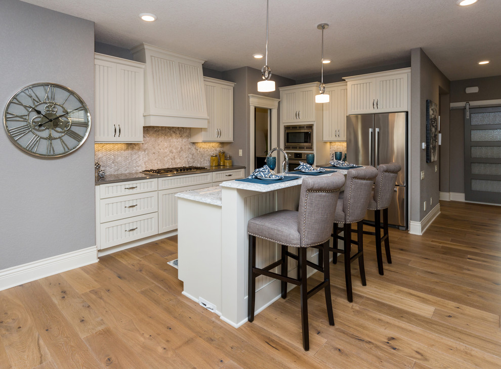 Transitional l-shaped kitchen pantry photo with a farmhouse sink, beaded inset cabinets, white cabinets, quartz countertops, beige backsplash, stone tile backsplash, stainless steel appliances and an island