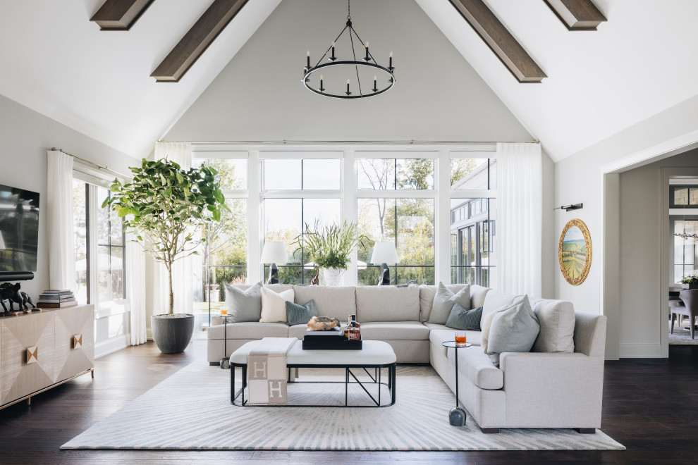 This is an example of a large transitional open concept family room in Chicago with white walls, dark hardwood floors, no fireplace, a wall-mounted tv, brown floor and exposed beam.