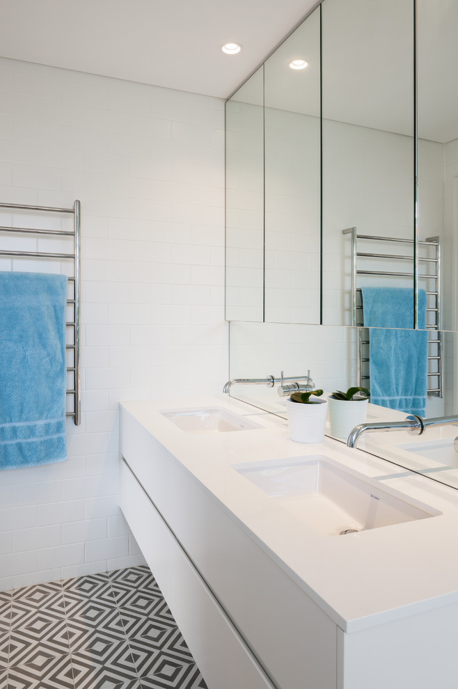 Photo of a beach style master bathroom in Sydney with an open shower, a wall-mount toilet, cement tile, an undermount sink, engineered quartz benchtops, flat-panel cabinets, white cabinets, white tile, white walls, cement tiles, grey floor and an open shower.