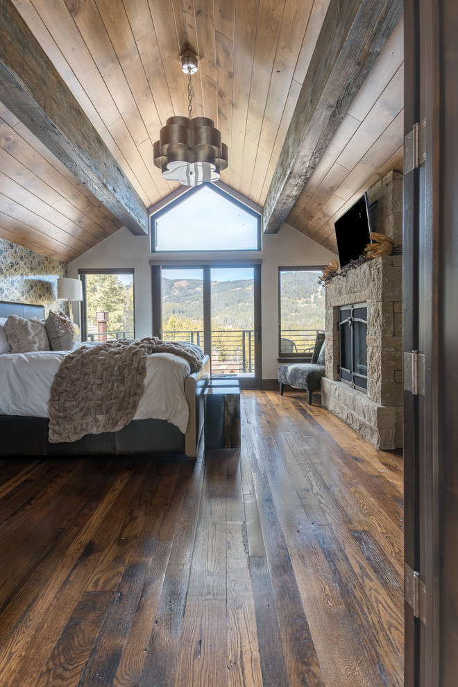 This is an example of a mid-sized country guest bedroom in Denver with white walls, medium hardwood floors, a standard fireplace, a stone fireplace surround and brown floor.