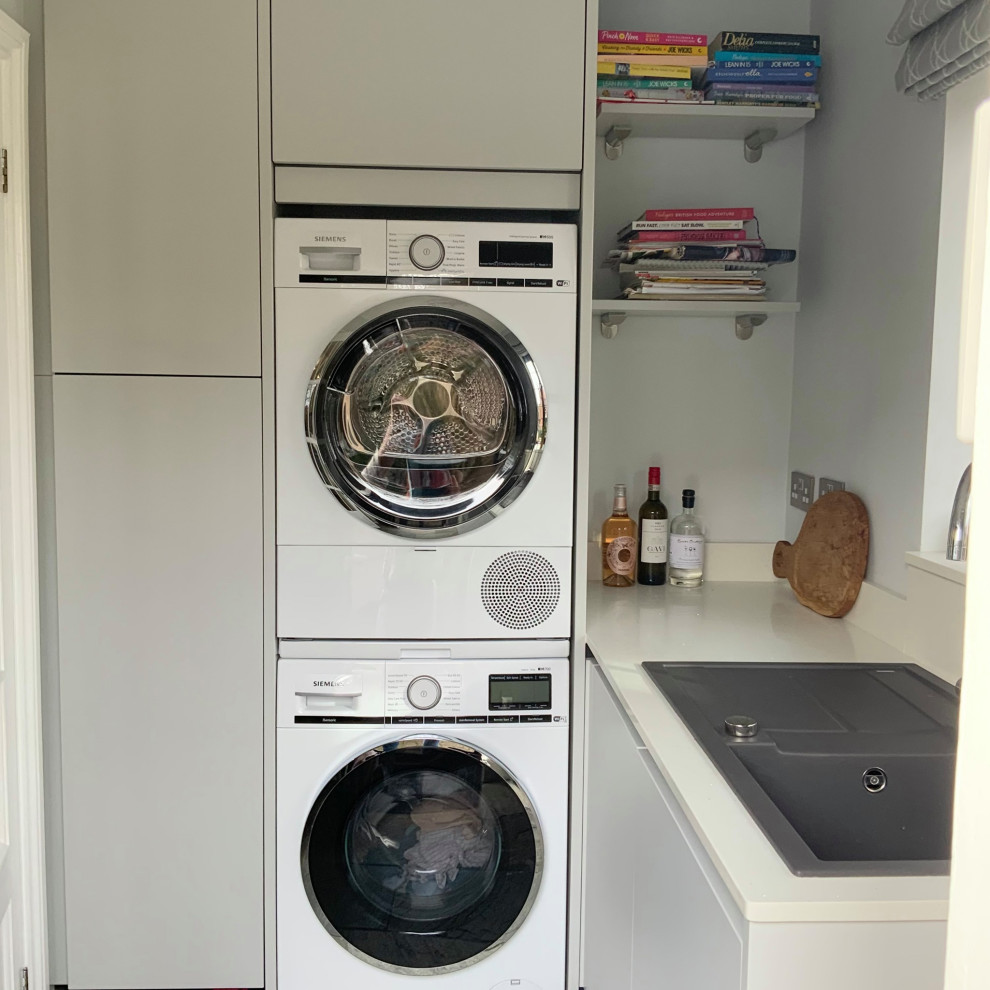 Mid-sized contemporary laundry room in Buckinghamshire with flat-panel cabinets, grey cabinets, quartzite benchtops, metallic splashback, mirror splashback and white benchtop.