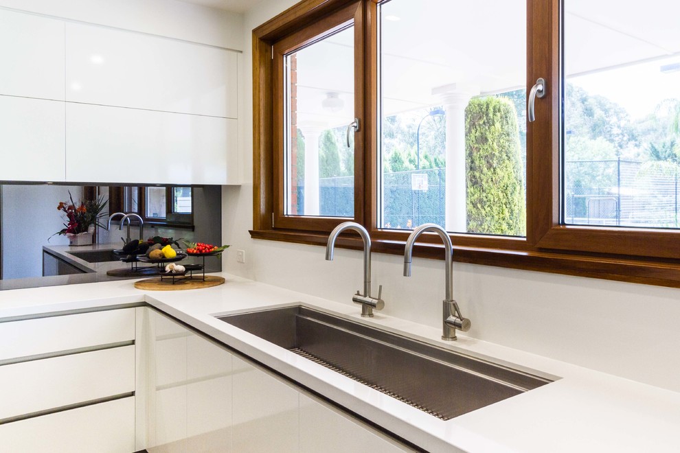 Inspiration for a large contemporary u-shaped eat-in kitchen in Melbourne with an undermount sink, flat-panel cabinets, quartz benchtops, mirror splashback, stainless steel appliances, medium hardwood floors and with island.