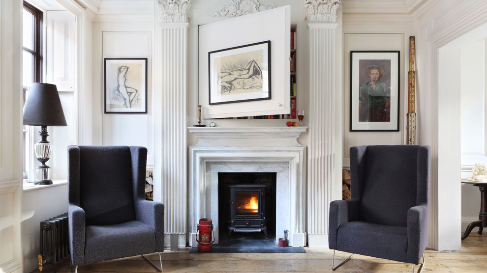 Design ideas for a traditional living room in London with a library, white walls, light hardwood floors and a wood stove.