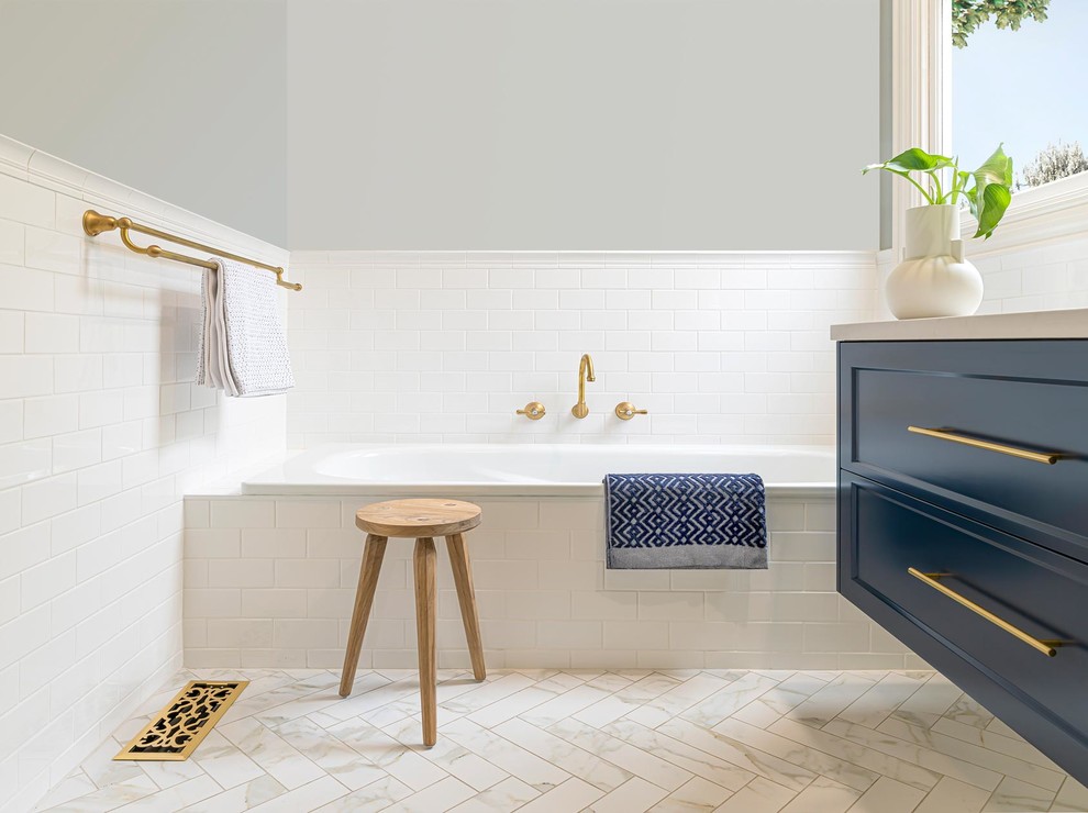 Mid-sized traditional 3/4 bathroom in Melbourne with shaker cabinets, blue cabinets, a drop-in tub, a curbless shower, a wall-mount toilet, white tile, ceramic tile, grey walls, porcelain floors, an undermount sink, engineered quartz benchtops, white floor, a hinged shower door and grey benchtops.