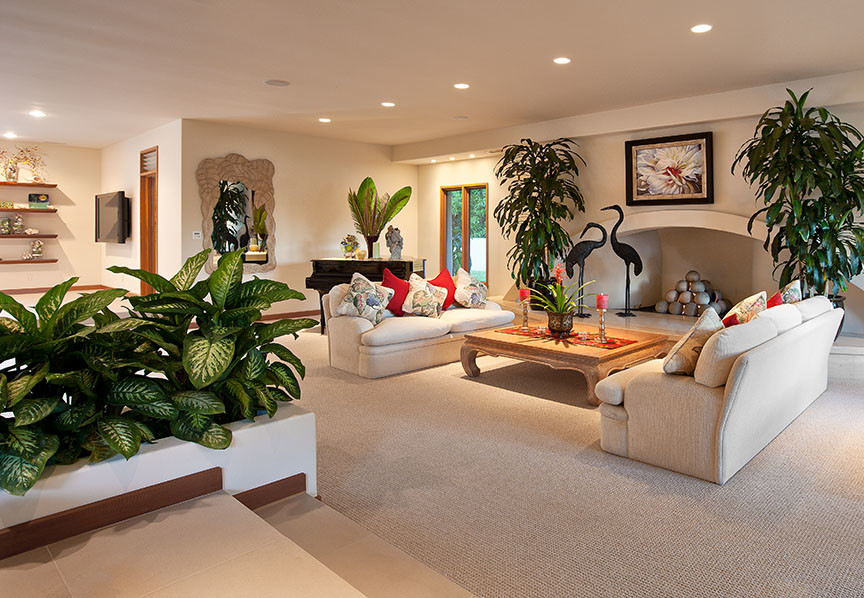 Large tropical open concept living room in Santa Barbara with a music area, beige walls, carpet, a wall-mounted tv, a standard fireplace, a plaster fireplace surround and beige floor.