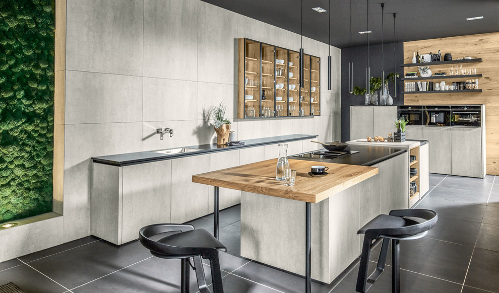 This is an example of a large contemporary galley eat-in kitchen in Other with a drop-in sink, ceramic splashback, black appliances, concrete floors, multiple islands, black floor, black benchtop, flat-panel cabinets, grey cabinets and grey splashback.
