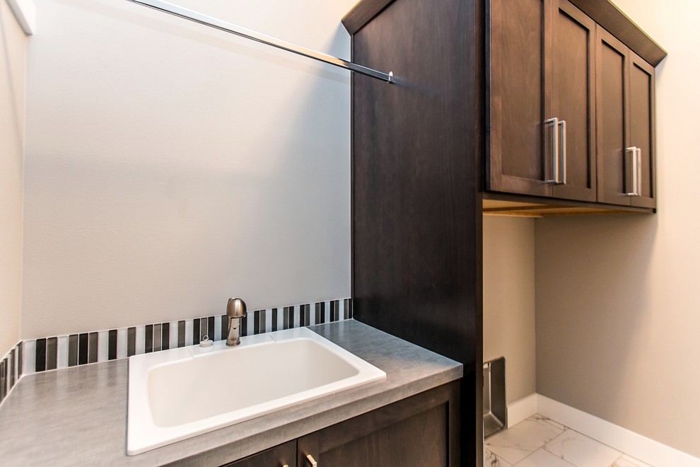 Photo of a small transitional single-wall dedicated laundry room in Seattle with an utility sink, shaker cabinets, dark wood cabinets, laminate benchtops, grey walls, marble floors, a side-by-side washer and dryer, white floor and grey benchtop.