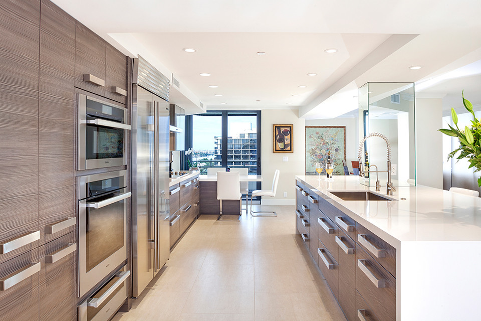 Design ideas for a large contemporary galley eat-in kitchen in Miami with a drop-in sink, flat-panel cabinets, medium wood cabinets, solid surface benchtops, stainless steel appliances, laminate floors, with island, beige floor and white benchtop.