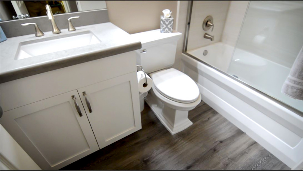 Photo of a small modern kids bathroom in Orange County with shaker cabinets, white cabinets, an alcove tub, a shower/bathtub combo, a two-piece toilet, beige tile, porcelain tile, beige walls, laminate floors, an undermount sink, engineered quartz benchtops, beige floor, a sliding shower screen and grey benchtops.