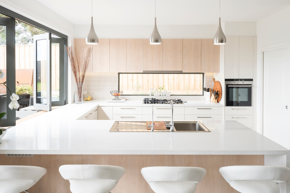 Photo of a mid-sized beach style u-shaped open plan kitchen in Geelong with a double-bowl sink, light wood cabinets, quartz benchtops, beige splashback, ceramic splashback, stainless steel appliances, porcelain floors and with island.