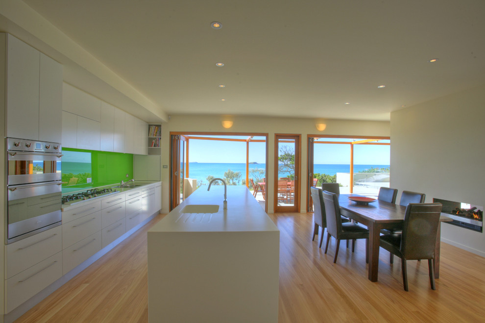 This is an example of a contemporary galley eat-in kitchen in Sydney with an integrated sink, flat-panel cabinets, green splashback and glass sheet splashback.