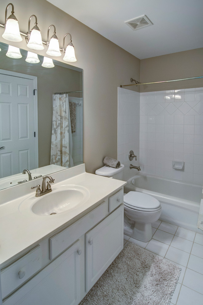 Mid-sized traditional master bathroom in Atlanta with raised-panel cabinets, white cabinets, an alcove tub, a shower/bathtub combo, a one-piece toilet, white tile, porcelain tile, beige walls, porcelain floors, an integrated sink and solid surface benchtops.