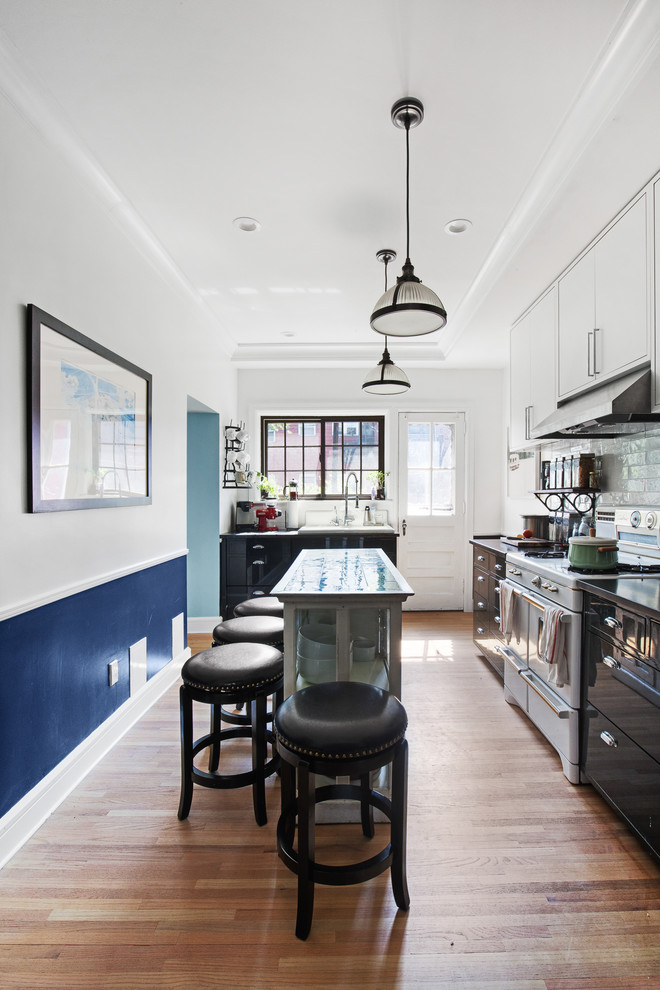Transitional single-wall kitchen in New York with flat-panel cabinets, white cabinets, white appliances, medium hardwood floors, with island and glass tile splashback.