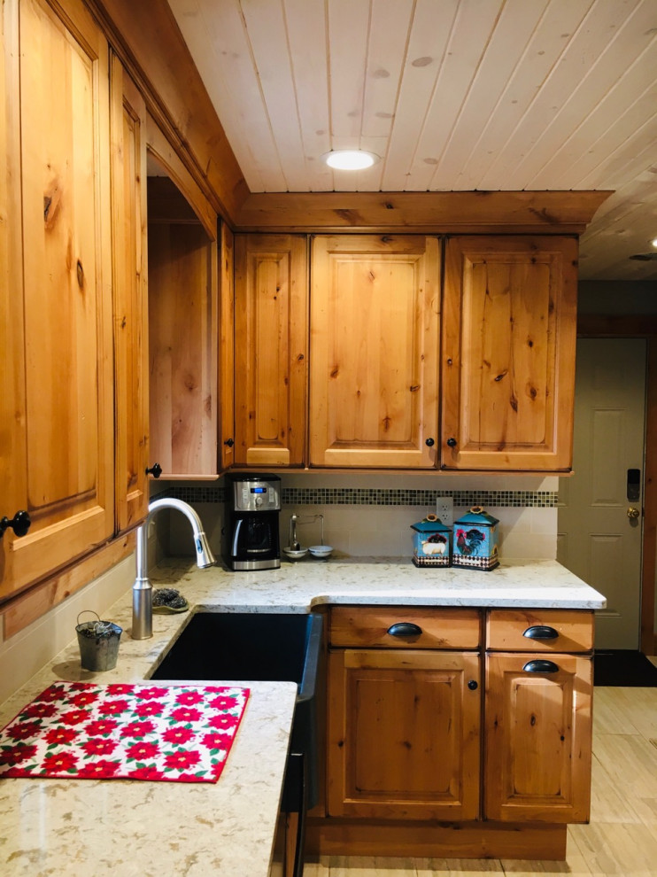 Inspiration for a mid-sized rustic u-shaped enclosed kitchen remodel with a farmhouse sink, raised-panel cabinets, light wood cabinets, quartz countertops, beige backsplash, limestone backsplash, stainless steel appliances and no island