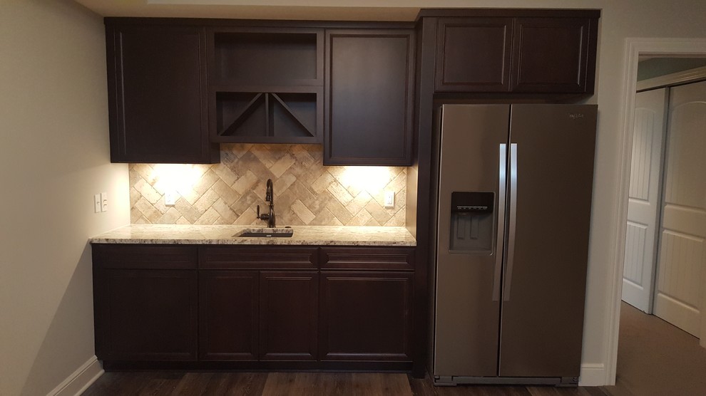This is an example of a transitional single-wall kitchen in Cleveland with an undermount sink, flat-panel cabinets, brown cabinets, granite benchtops, beige splashback, travertine splashback, dark hardwood floors and brown floor.